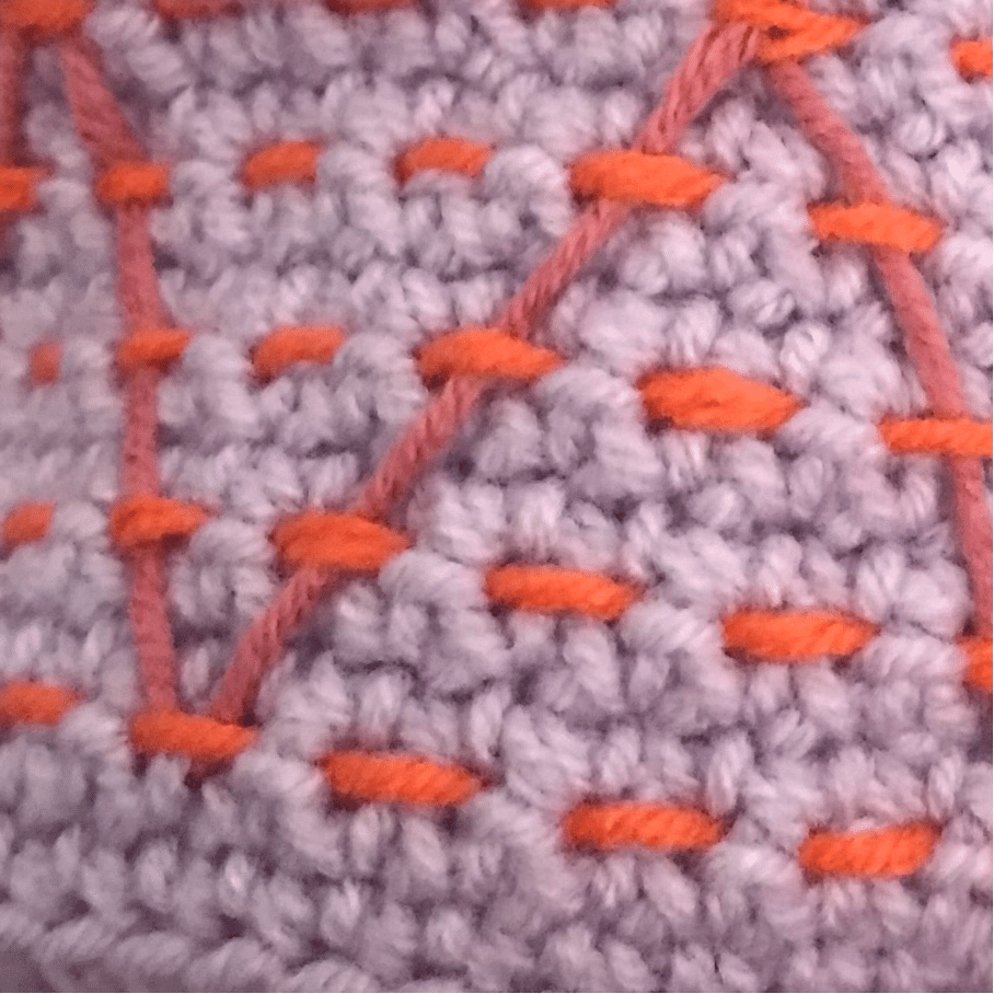 haakwerk in lila met kleurrijk borduurpatroon er op, in kleine steken.