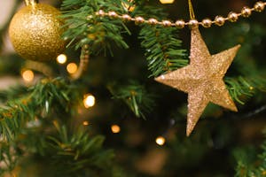 Close-up of a Christmas tree with golden star and ornament, shimmering lights and festive decorations.